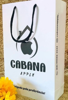 Sacola de papel branca, com a logomarca da Caban Apple (a logomarca consiste em um desenho da logomarca da Apple, que é uma maçã, e envolta desse maçã tem um desenho de uma casa, simbolizando a cabana).