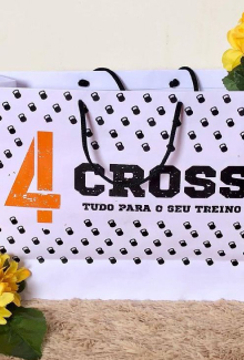 Sacola de papel colorida, com a logomarca da Cross (A logomarca consiste em uma palavra Cross e ao lado esquerdo dessa palavra, tem um número quatro bem grande na cor laranja). Cross, tudo para o seu treino.