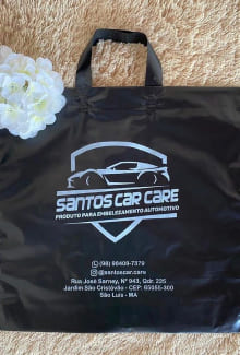 Sacola plástica alça fita na cor preta, com a logomarca Santos Car Care (a logomarca consiste na frase Santos Car Care e em cima dessa frase, tem o desenho de um carro).